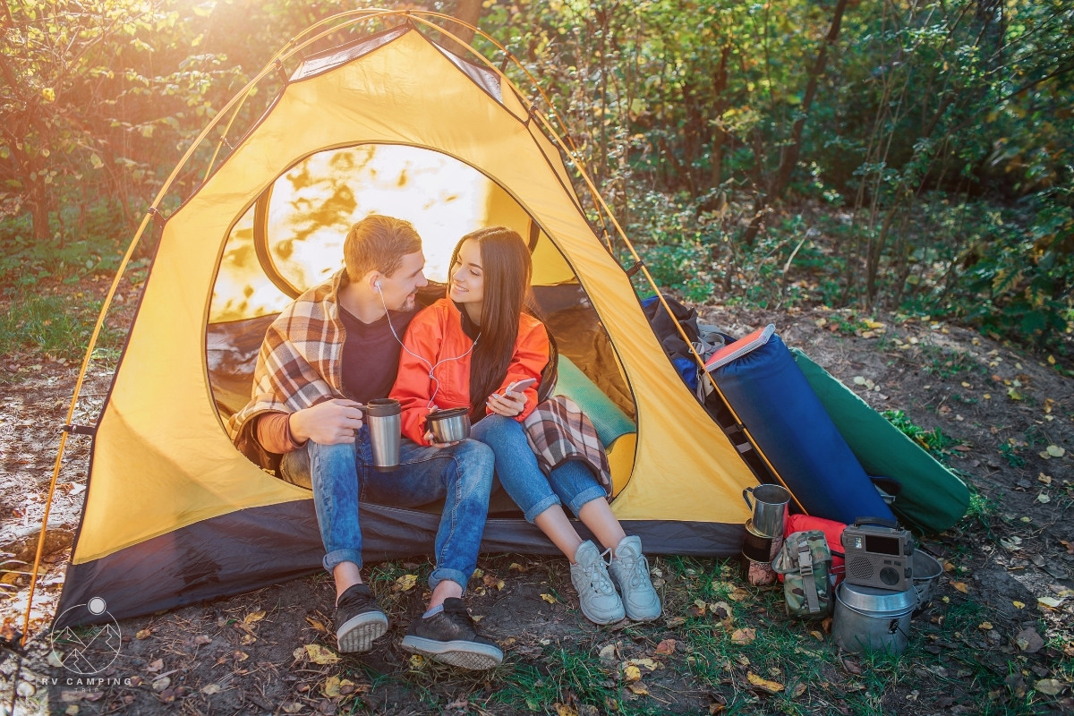 couple sitting in tent listening to music through headphones and holding coffee mugs