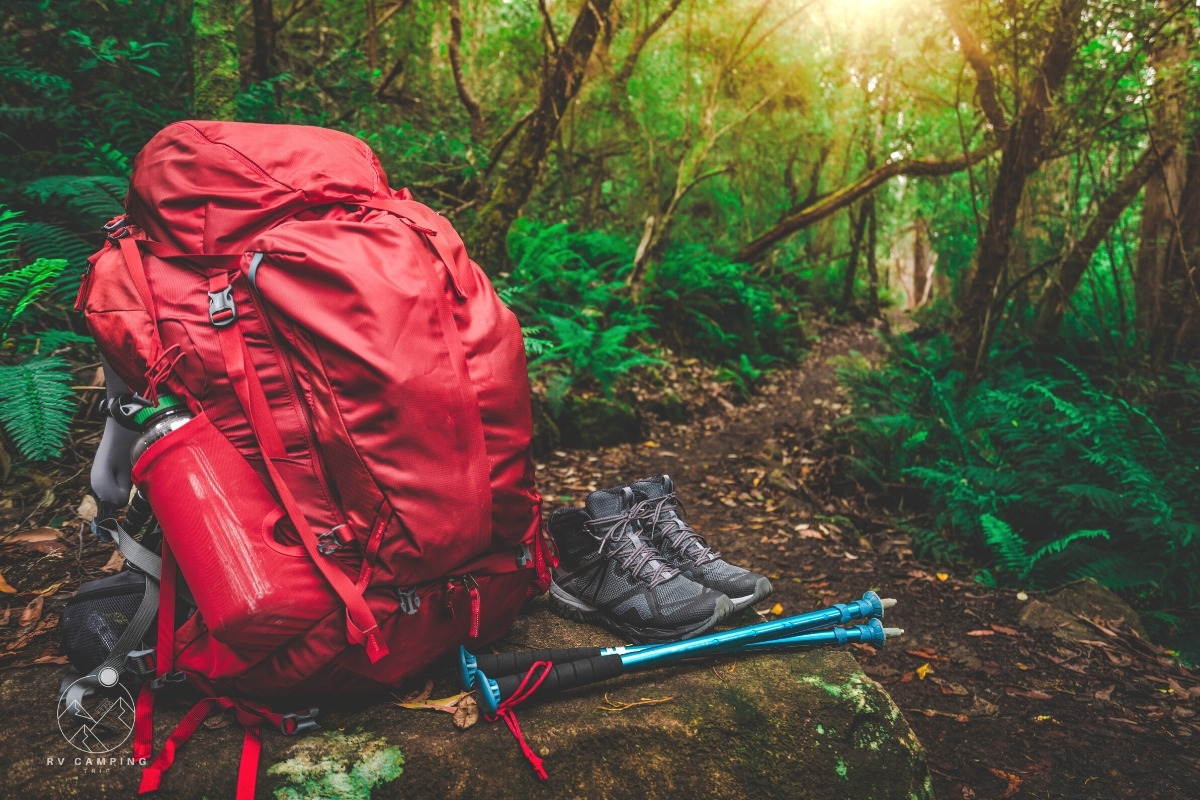 red backpack filled with hiking gear beside pair of hiking boots in rainforest