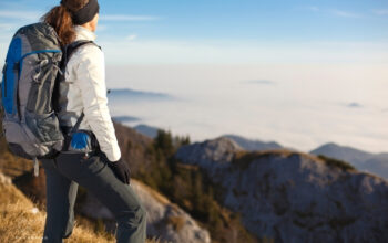 young woman standing on mountain top wearing hiking gear