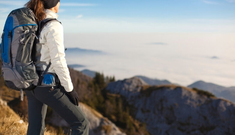 young woman standing on mountain top wearing hiking gear