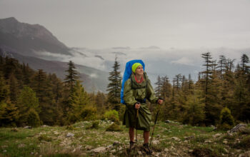 Girl in the raincoat standing with hiking backpack and sticks