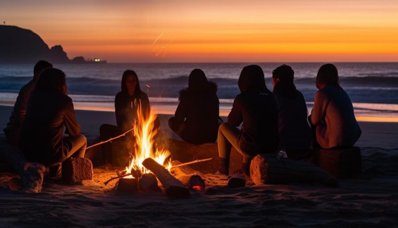 Photo a group of people sit around a campfire on the beach at sunset.